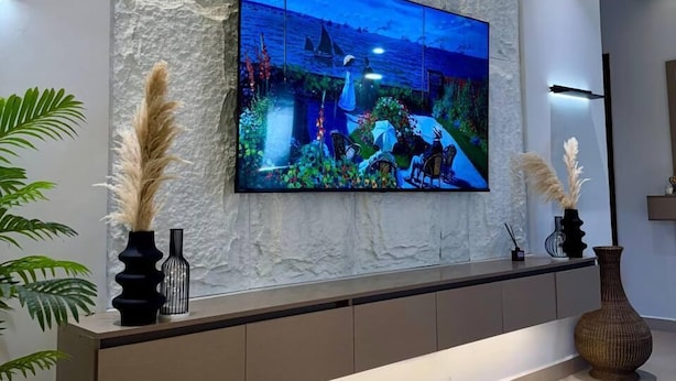 A modern living room with a large flat-screen TV mounted on a textured wall, a sleek console table with decorative vases, and a minimalist design. - Ace Homes Bubga 3BR (Kampala)