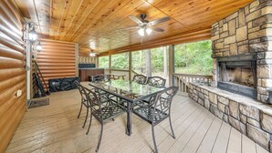 A covered outdoor deck with a stone fireplace, wooden ceiling, and a glass-top table surrounded by chairs. - Pets & Families Welcome: Secluded Broken Bow Cabin (Broken Bow)