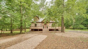 A rustic cabin with a wooden deck, surrounded by trees and gravel paths. - Pets & Families Welcome: Secluded Broken Bow Cabin (Broken Bow)