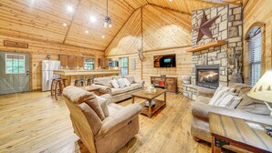 A spacious log cabin interior with a stone fireplace, a kitchen area, and a cozy seating arrangement. - Pets & Families Welcome: Secluded Broken Bow Cabin (Broken Bow)