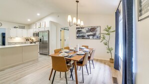 Eine moderne Küche mit weißen Schränken, einer zentralen Kochinsel, Edelstahlgeräten und einem Essbereich mit Holztisch und Stühlen.