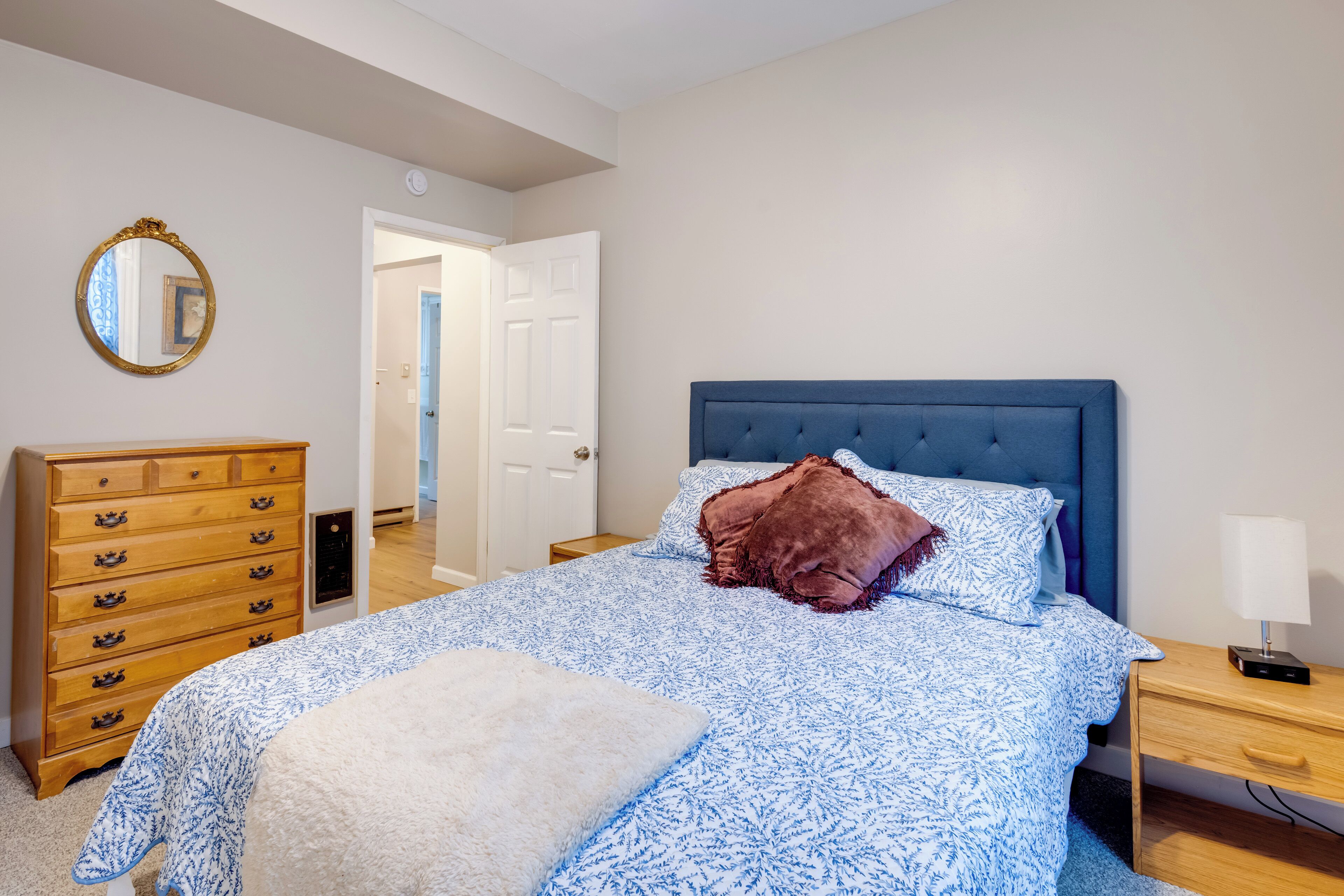 A bedroom with a large bed, a wooden dresser, a nightstand, and a mirror on the wall.