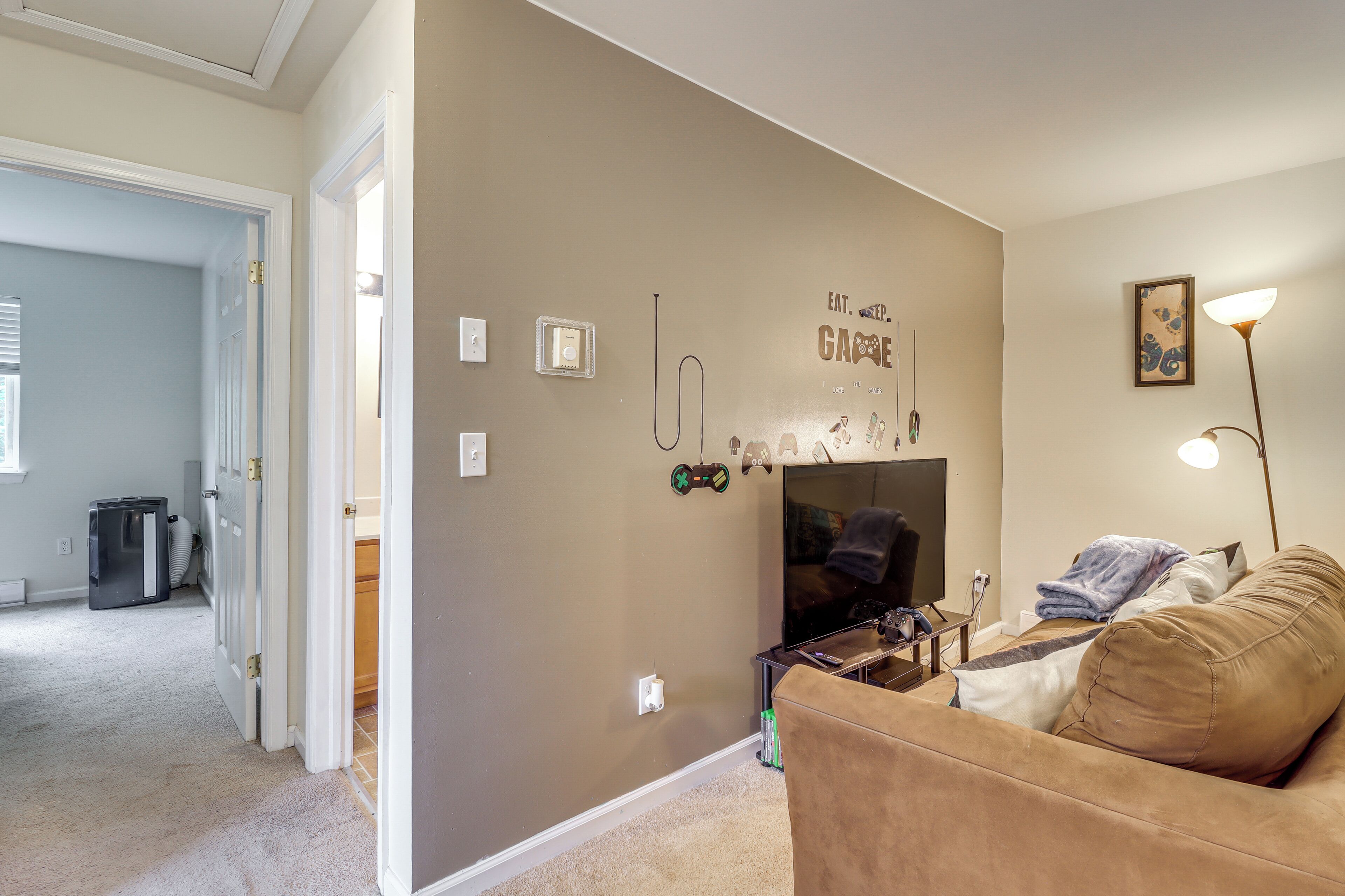 A living room with a beige wall, a brown couch, a TV, and a lamp.