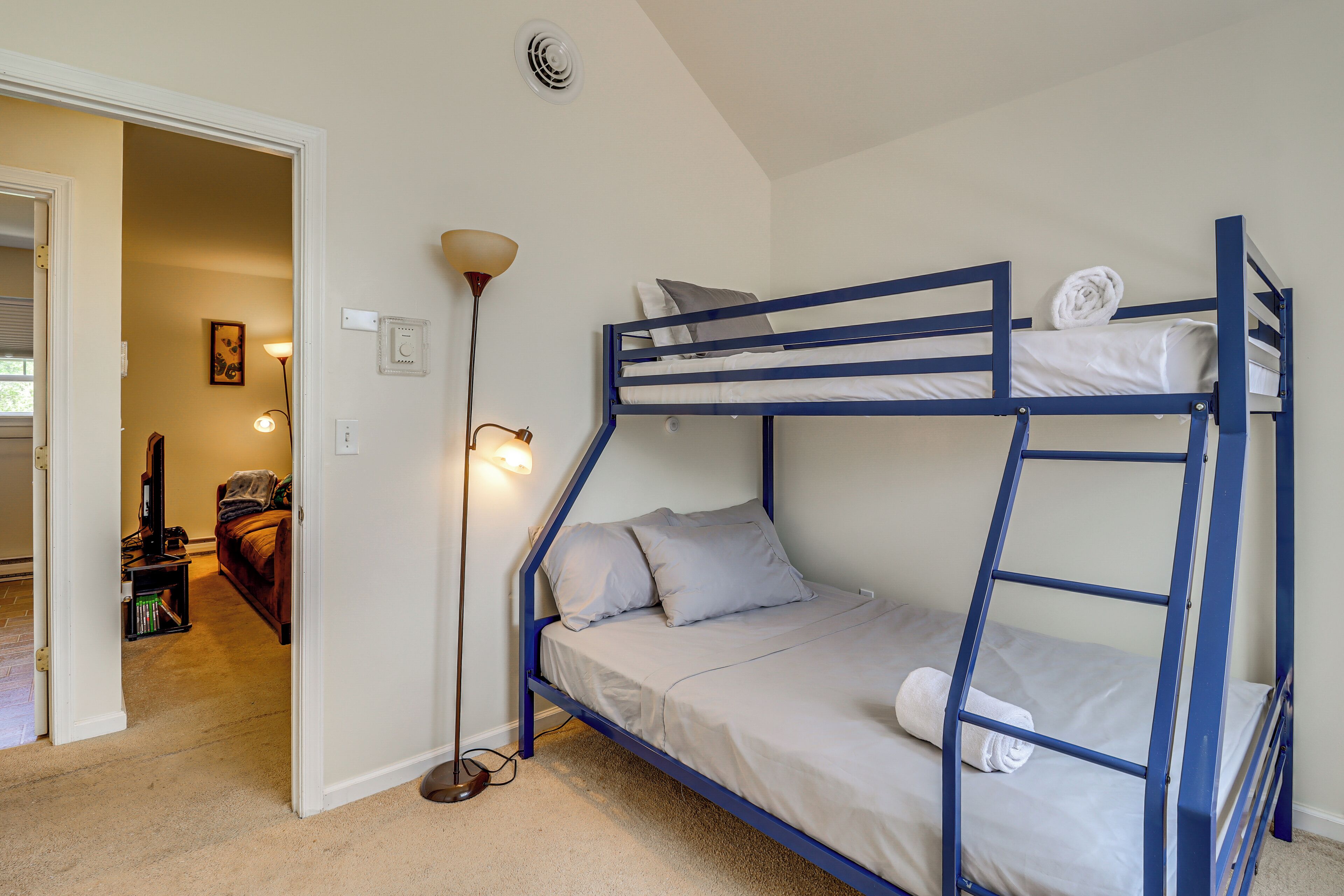 A bunk bed with a ladder, a floor lamp, and a door leading to another room.
