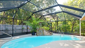 A covered swimming pool with a stone feature, surrounded by a wooden fence and trees. - Private Backyard Oasis: Cocoa Family Home! (Cocoa)