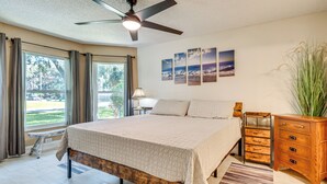 A bedroom with a bed, a wooden nightstand, a ceiling fan, and a window with curtains. - Private Backyard Oasis: Cocoa Family Home! (Cocoa)