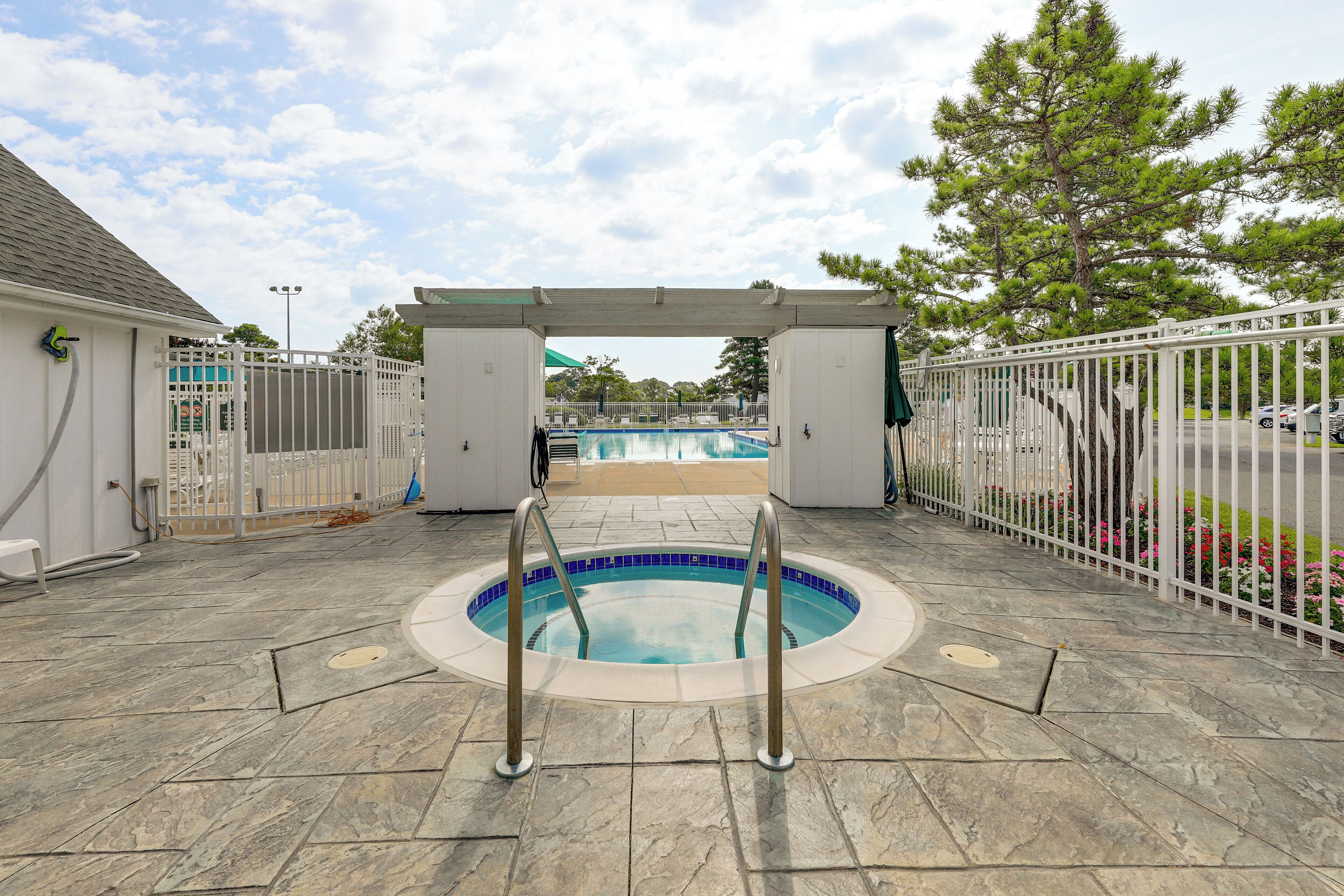 A circular pool with a white fence and metal railings, surrounded by stone tiles and a pergola structure.