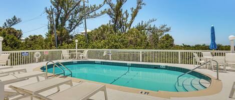 A rectangular swimming pool with a deck area, surrounded by a white fence, and trees in the background.