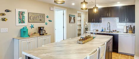 A kitchen with a marble island, pendant lighting, and a coffee sign on the wall.