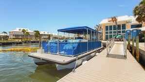 Un bateau amarré, doté d’un espace de repos couvert, d’une passerelle en bois et d’un bâtiment avec des fenêtres et une porte en arrière-plan.