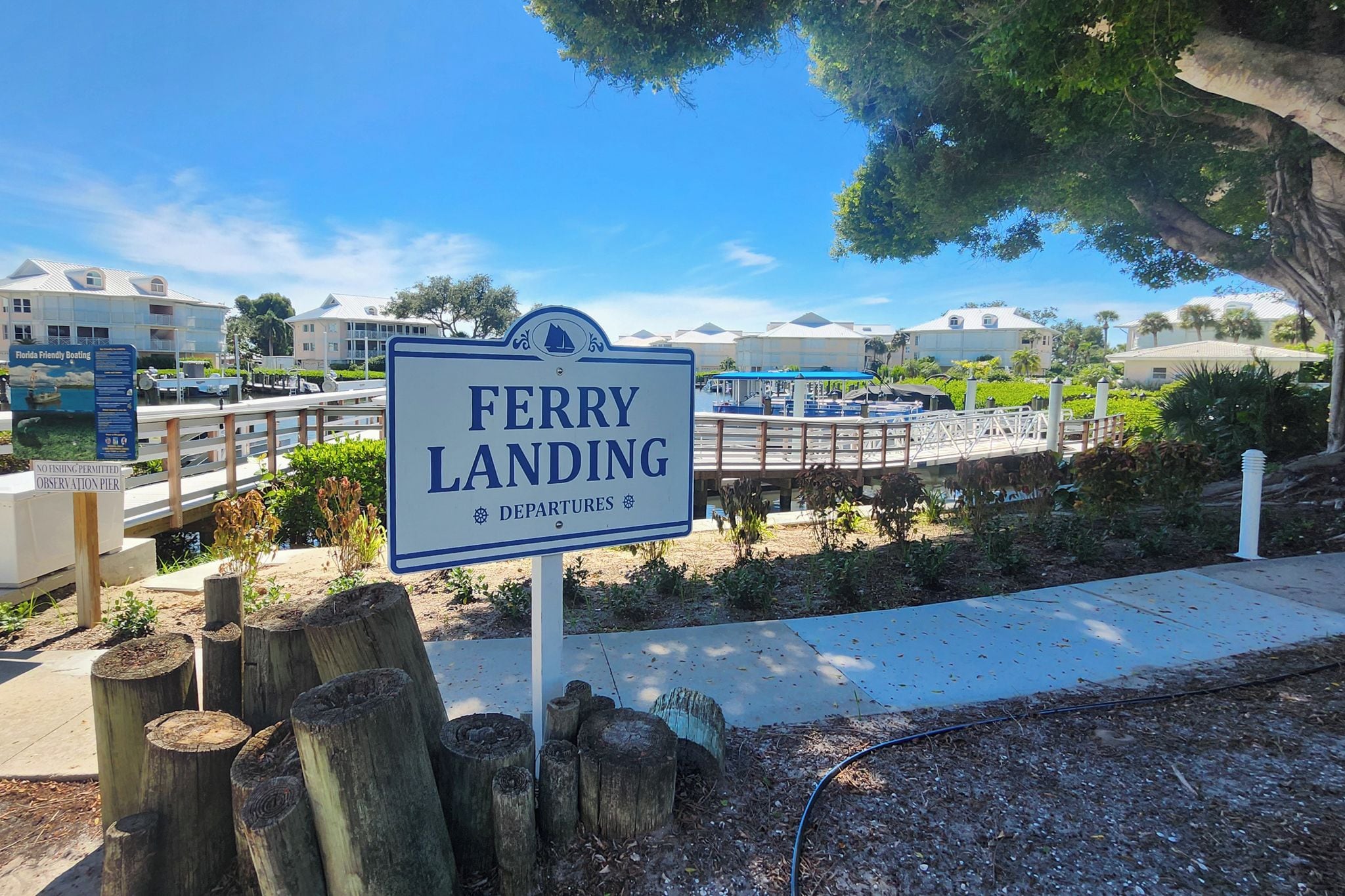 A sign for a ferry landing with a view of a marina and buildings in the background.