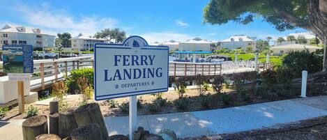 A sign for a ferry landing with a view of a marina and buildings in the background.