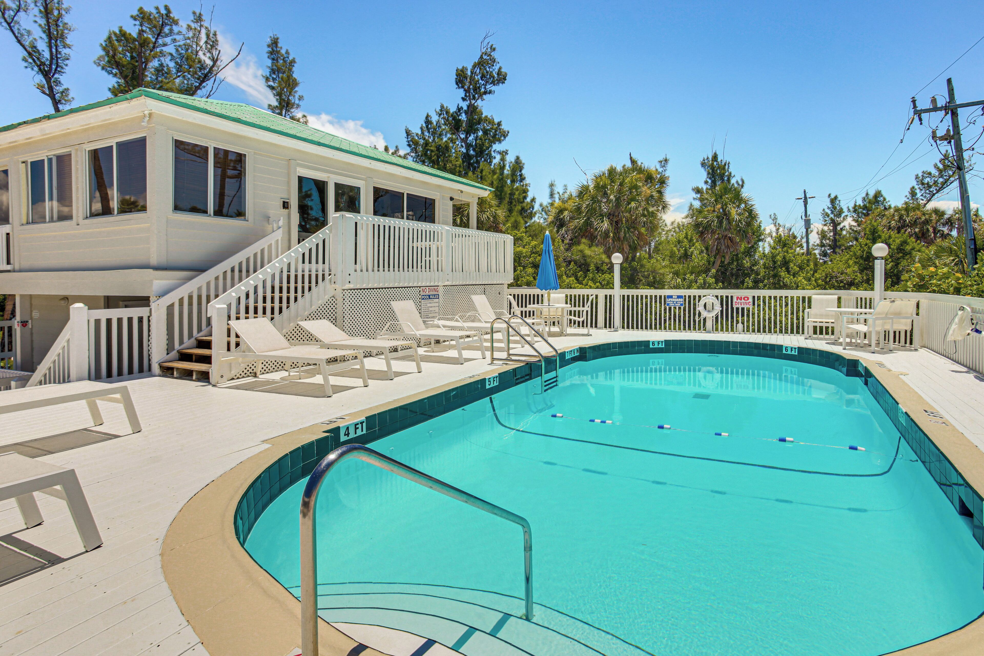 A swimming pool with a white deck, a covered seating area, and a building with a green roof.