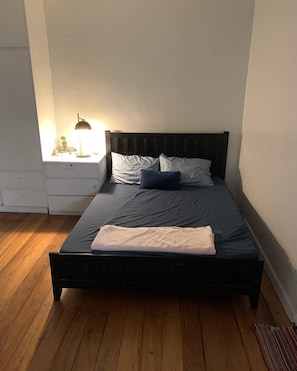 A bed with a dark headboard, a bedside table with a lamp, and a small plant.