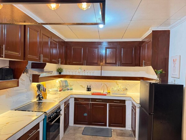 Una cocina con armarios de madera oscura, encimera de mármol, horno integrado y refrigerador negro.