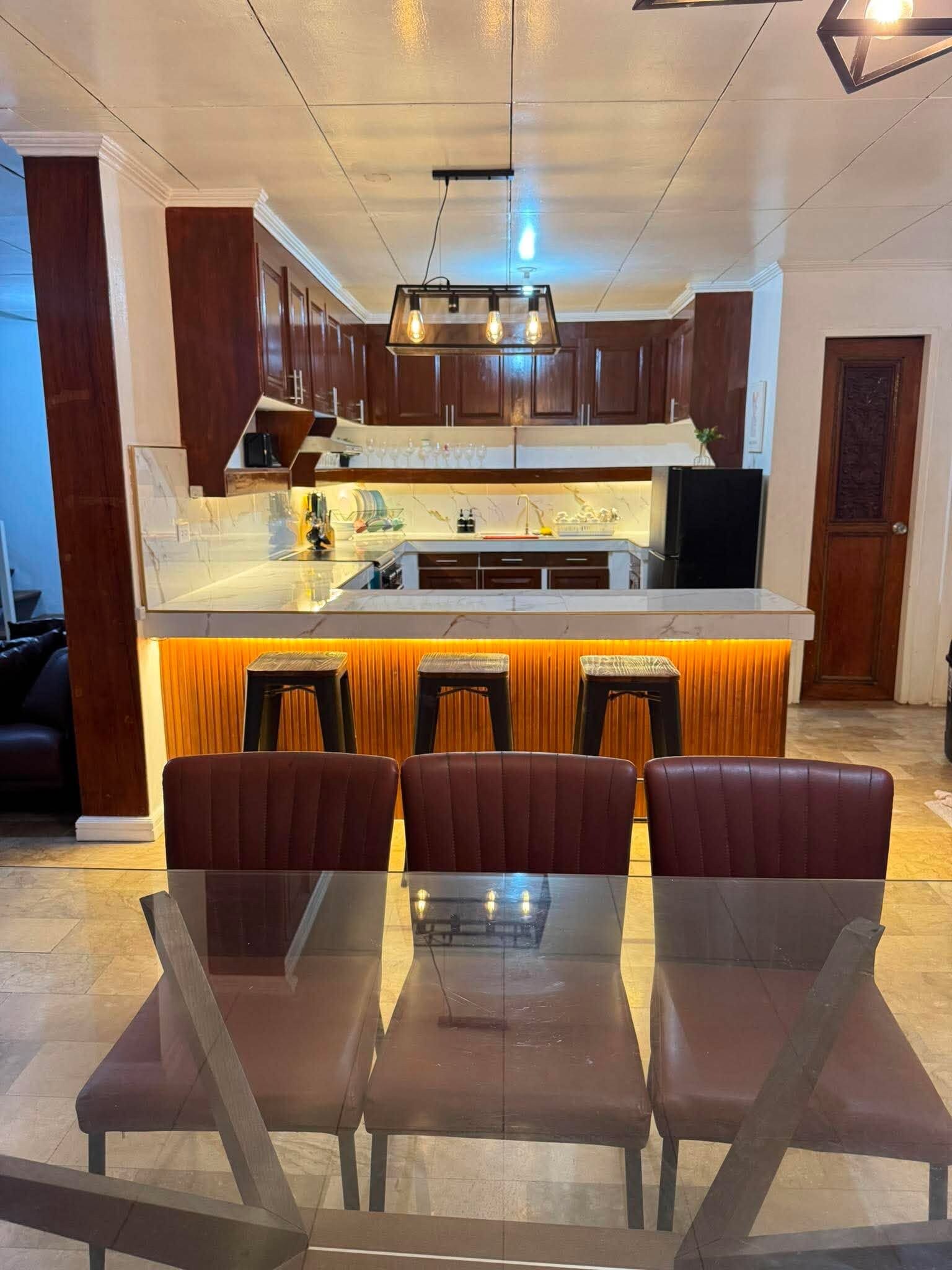 A modern kitchen with a central island, bar stools, and a dining table.