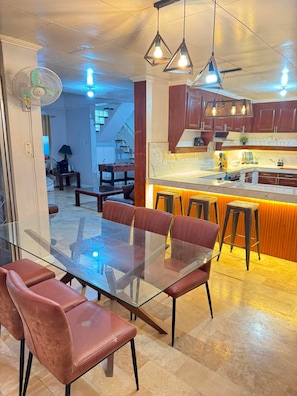 Una cocina moderna con una mesa de comedor de vidrio y sillas rojas, una barra con taburetes e iluminación colgante.