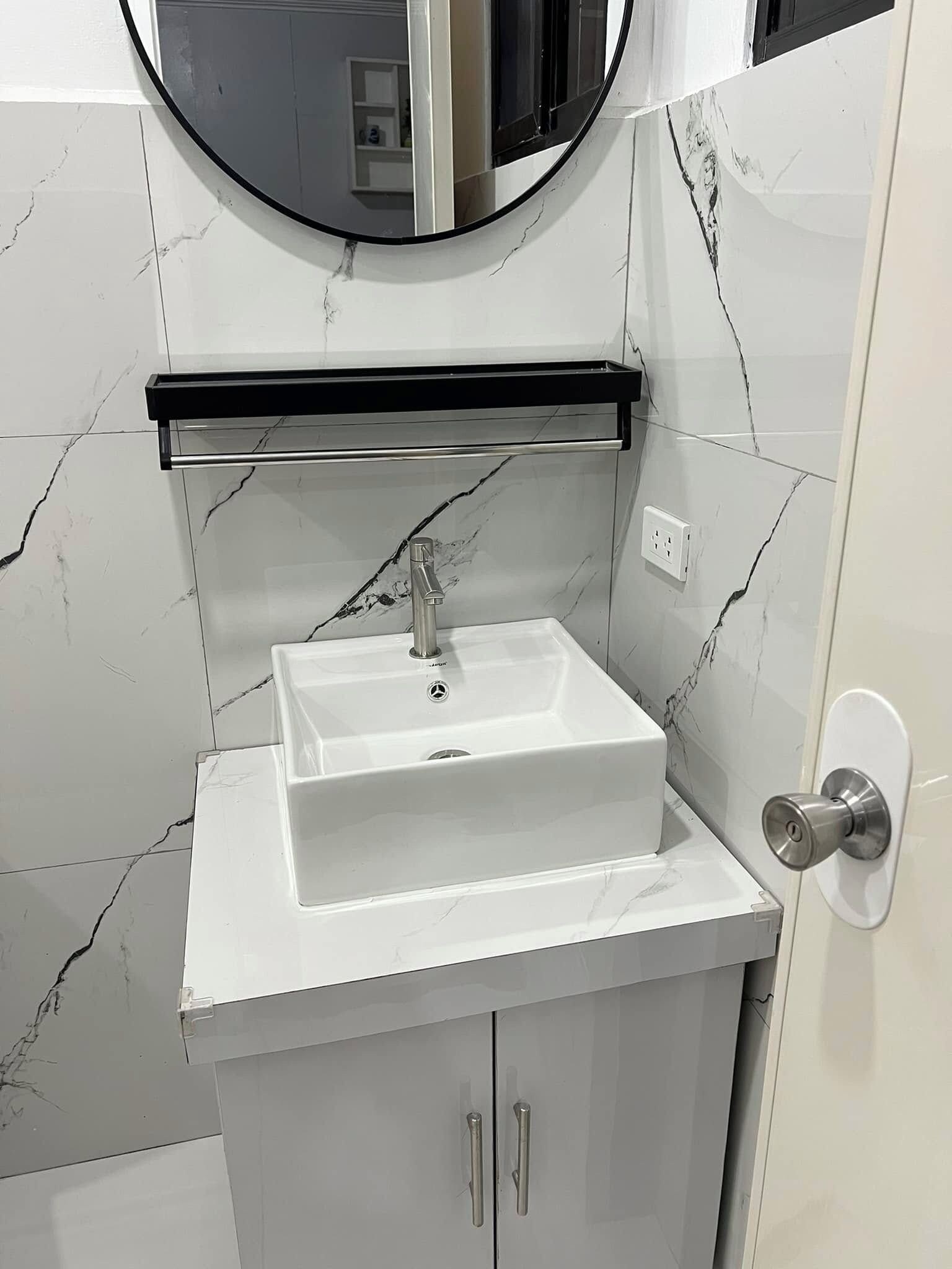 A bathroom with a white sink, a mirror above it, and a marble-patterned wall.
