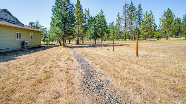 A house with a gravel driveway, surrounded by a fenced yard with tall pine trees. - Fish, Raft & Hike: Southwest OR Couples Retreat! (Trail)