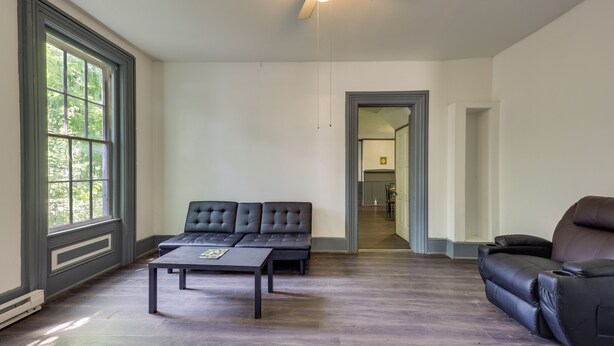 A spacious living room with a dark wood floor, a black leather sofa, a black leather recliner, and a coffee table. - Walk to Dtwn Bath: Apt Near Keuka Lake & Wine Trl (Bath)
