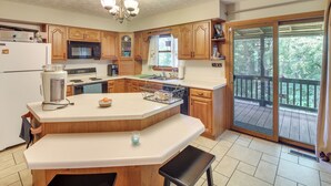 A kitchen with wooden cabinets, a white countertop, a built-in oven, a microwave, and a large window overlooking a deck. - Family Home w/ Game Room! 1 Mi to Dale Hollow Lake (Burkesville)