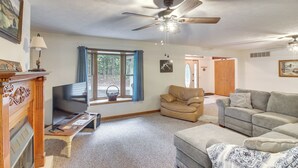 A living room with a fireplace, a television, a ceiling fan, and a large window with curtains. - Family Home w/ Game Room! 1 Mi to Dale Hollow Lake (Burkesville)
