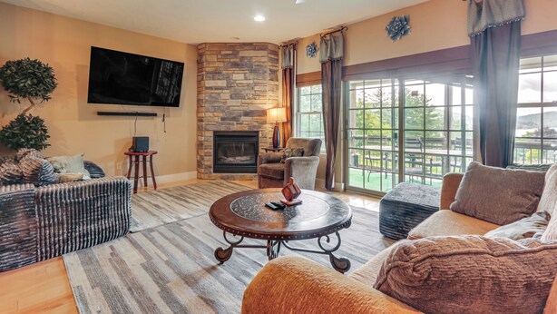 A living room with a stone fireplace, a flat-screen TV, a round coffee table, and a large window with curtains. - 1 Mi to Wisp Resort: Hot Tub Haven in Mchenry! (McHenry)
