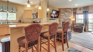 A kitchen with a large island, bar stools, wooden cabinets, a microwave, and a stone fireplace. - 1 Mi to Wisp Resort: Hot Tub Haven in Mchenry! (McHenry)