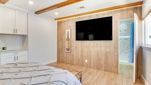 A bedroom with a bed, wooden flooring, a mounted TV, a painting, and a bathroom with a shower. - Hacienda Heights Gem w/ Large Patio! (Hacienda Heights)