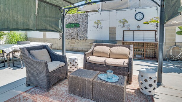 A covered outdoor seating area with wicker furniture, a table, and a decorative wall with a clock. - Hacienda Heights Gem w/ Large Patio! (Hacienda Heights)
