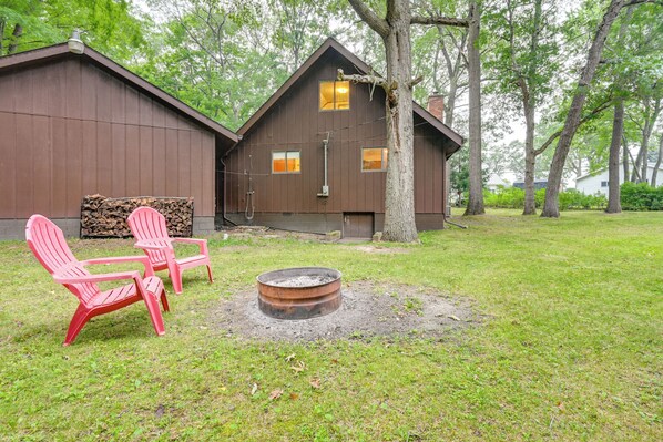 Une cabane rustique avec un foyer et deux chaises Adirondack dans la cour.