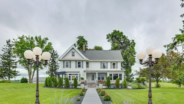 A two-story house with a front porch, a pathway leading to the entrance, and a lawn with trees and shrubs. - Fire Pits, Views & Yard: Luxe Mt Horeb Getaway! (Mount Horeb)