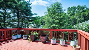 Une terrasse en bois avec une rambarde rouge, entourée d’arbres et de plantes en pot.