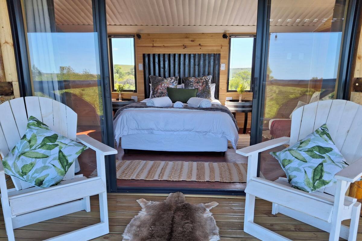A bedroom with a large bed, two white chairs with patterned cushions, and a fur rug on the floor.