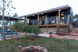 A rustic cabin with a wooden deck, outdoor seating, and a staircase leading to the entrance. - Coopers Highlands  (Jeffreys Bay)