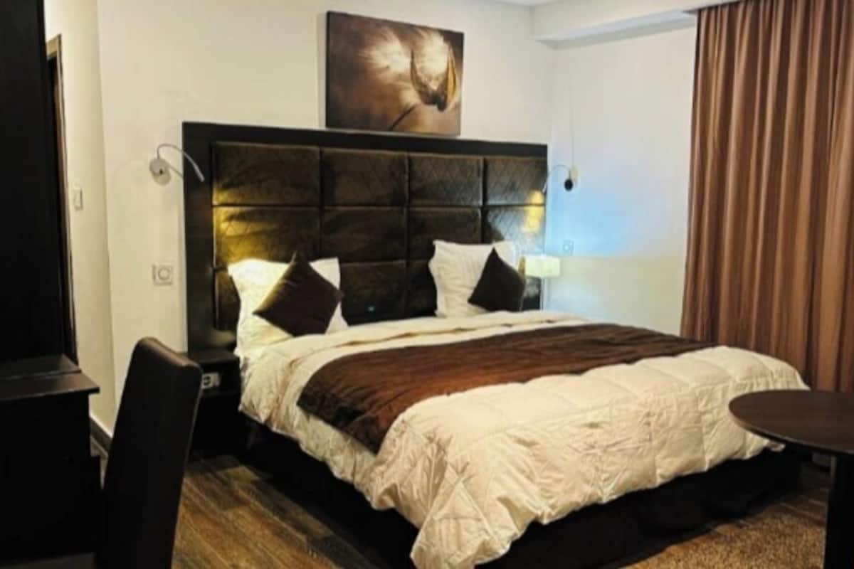 Ein Hotelzimmer mit einem großen Bett, einem Kopfteil, einem Schreibtisch und einem Stuhl.