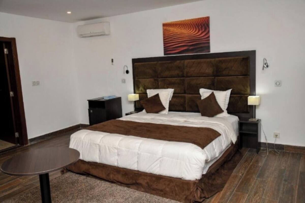 Ein Schlafzimmer mit einem großen Bett, einem Nachttisch, einer Wand-Klimaanlage und einem Gemälde über dem Bett.