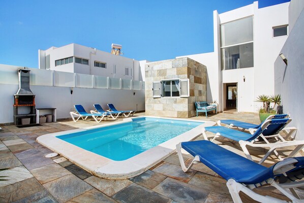 A swimming pool with lounge chairs, a barbecue grill, and a modern building with large windows.