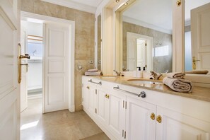 A bathroom with a large mirror, a sink, and a door leading to another room.