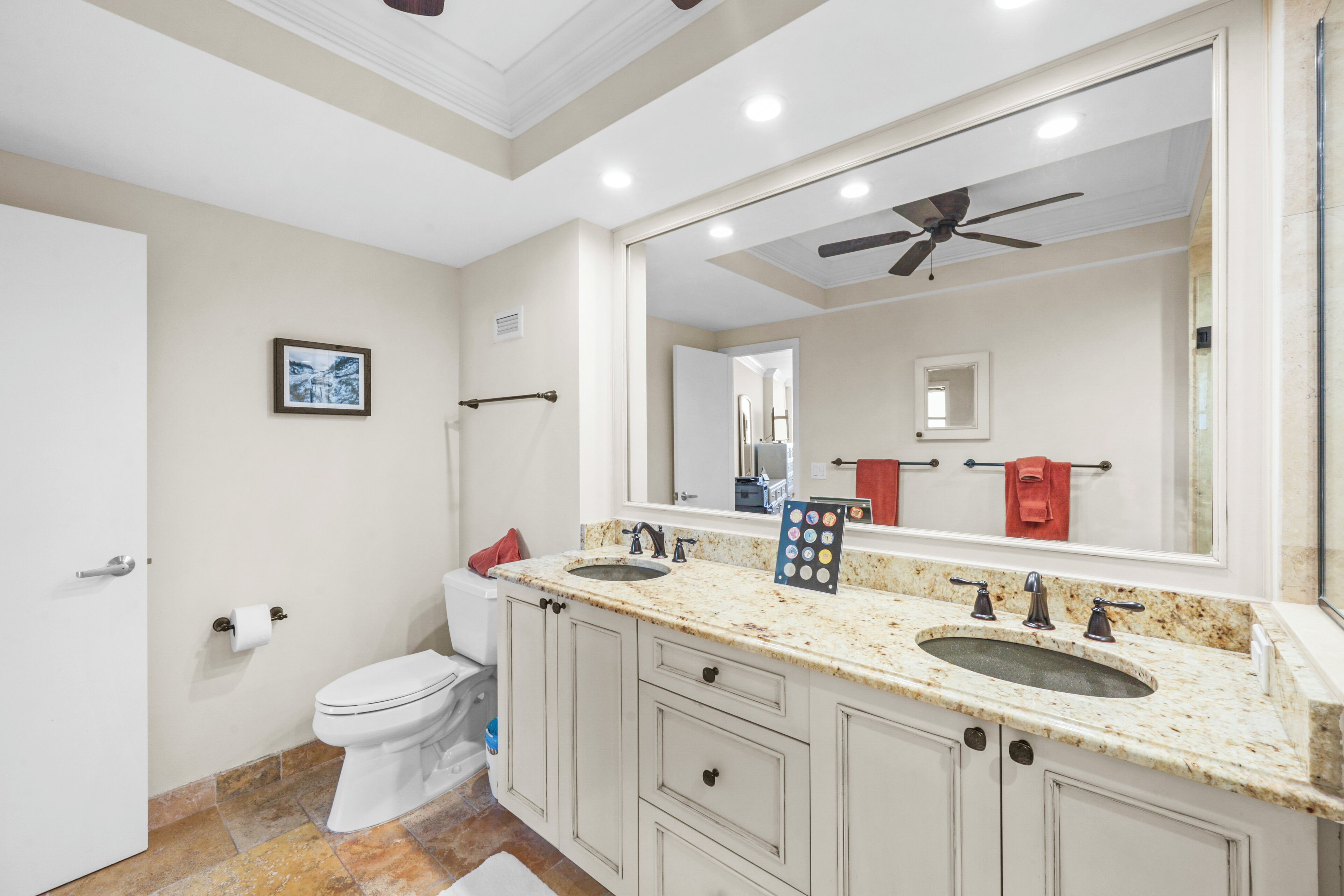 A modern bathroom with a double sink vanity, a large mirror, and a ceiling fan.