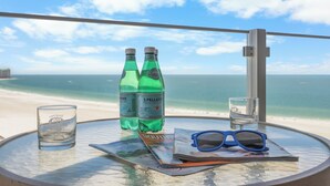Una mesa con dos botellas de agua carbonatada S.Pellegrino, un vaso y un par de gafas de sol, con vista a la playa.
