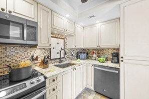 A modern kitchen with white cabinetry, a stainless steel microwave, a stove, and a dishwasher. - 18th Floor Beachfront Condo | Pool, Gym & Grills (Marco Island)