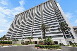 Un hotel alt amb nombrosos balcons, un pati paisatjístic amb palmeres i un cel blau i clar.