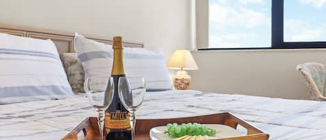 A bed with a wooden tray containing a bottle of champagne, two glasses, and a plate with grapes and crackers.