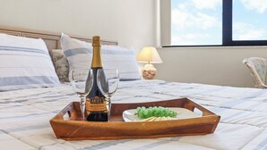 Una cama con una bandeja de madera que sostiene una botella de champán, dos copas y un plato de uvas.