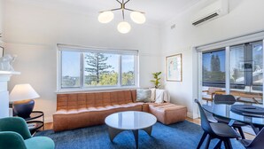 A modern living room with a leather sofa, a glass coffee table, and a dining area with a glass table and chairs.