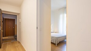 Ein Flur, der zu einem Schlafzimmer mit Bett, Tür und Lichtschalter an der Wand führt.