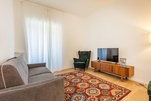 A living room with a sofa, a green armchair, a TV on a wooden cabinet, and a patterned rug.