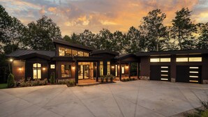 A modern two-story house with a large driveway, multiple garage doors, and a well-lit entrance.