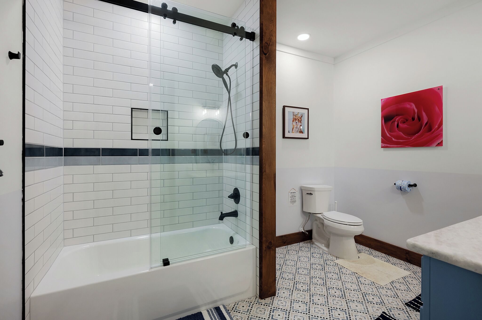 A modern bathroom with a glass-enclosed shower, white tiled walls, a white toilet, and a red rose artwork on the wall.